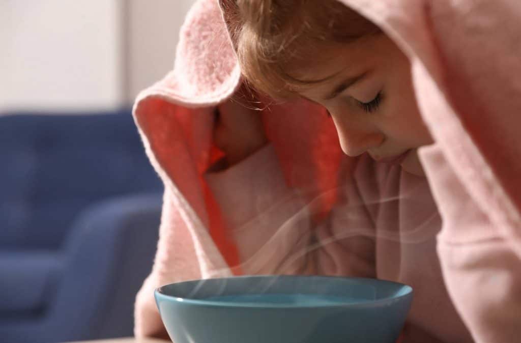 petite fille qui respire un bol d'eau chaude et d'huile essentielle