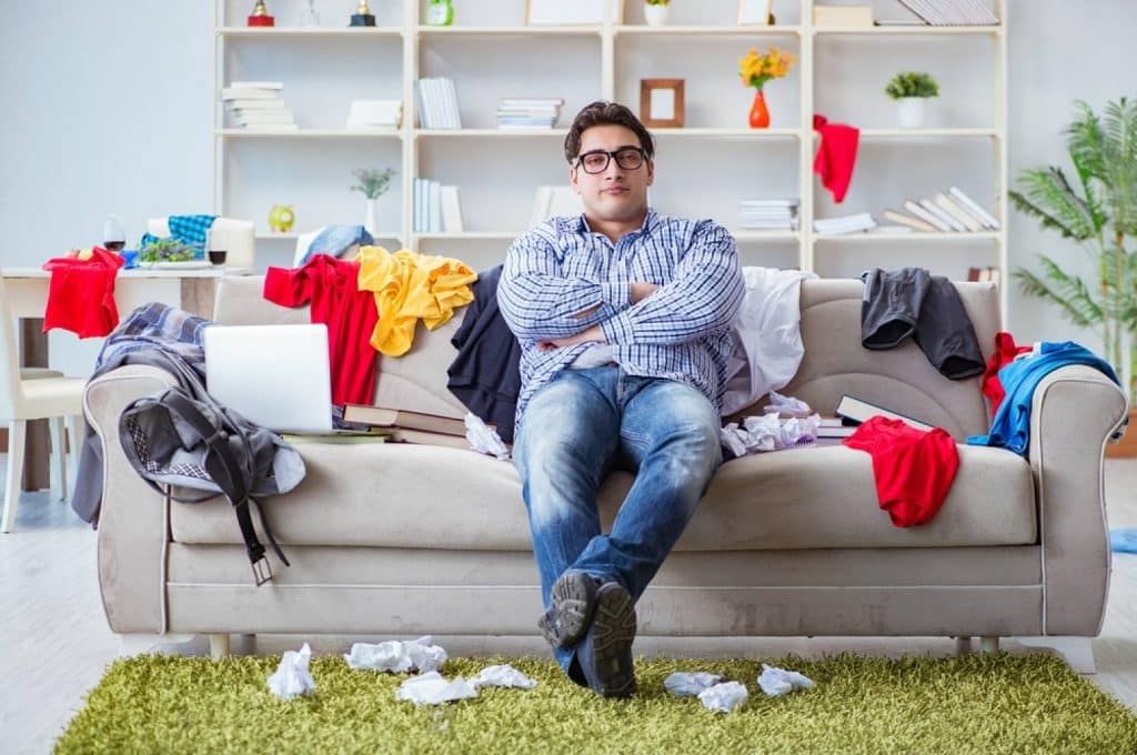 homme assis sur son canapé avec des affaires en désordre