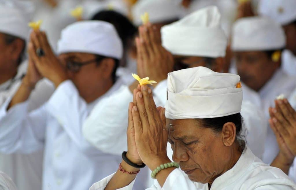 des balinais qui prient leur dieu avec une fleur de frangipanier dans les mains et vêtus de blanc