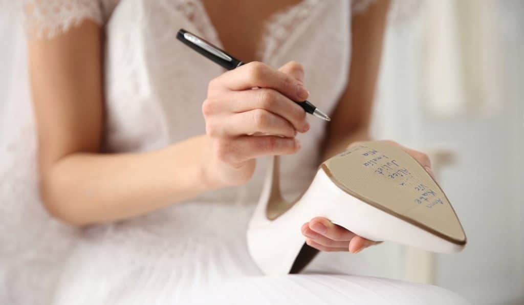 mariée qui écrit avec un stylo les prénoms sur sa chaussure le jour du mariage